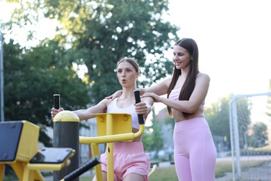 Photo of Young woman exercising with outdoor gym equipment with professional personal trainer outdoors