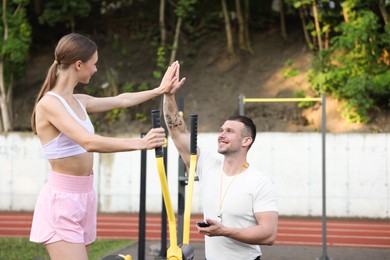 Photo of Young woman with professional personal trainer giving high five in outdoor gym