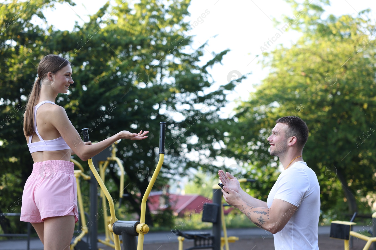 Young woman exercising with outdoor gym equipment with professional personal trainer outdoors Photo of Young woman exercising with outdoor gym equipment with professional personal trainer outdoors