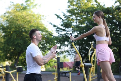 Photo of Young woman exercising with outdoor gym equipment with professional personal trainer outdoors