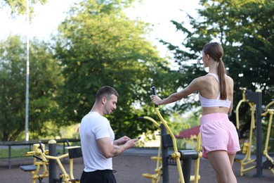 Photo of Young woman exercising with outdoor gym equipment with professional personal trainer outdoors