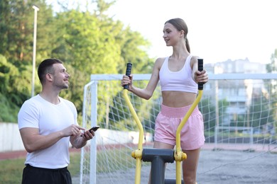 Photo of Young woman exercising with outdoor gym equipment with professional personal trainer outdoors