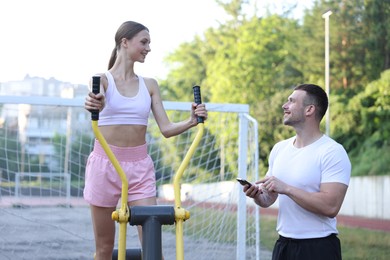 Photo of Young woman exercising with outdoor gym equipment with professional personal trainer outdoors