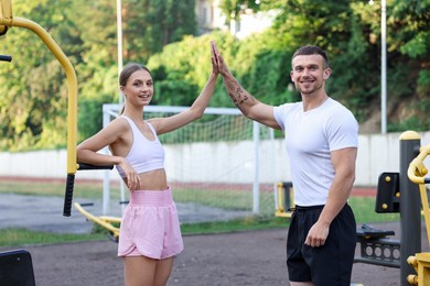Photo of Young woman with professional personal trainer giving high five in outdoor gym