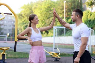 Photo of Young woman with professional personal trainer giving high five in outdoor gym