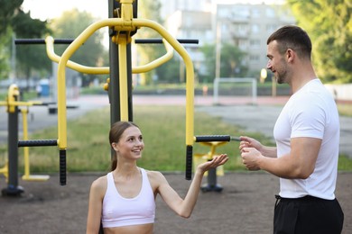 Photo of Young woman exercising with outdoor gym equipment with professional personal trainer outdoors