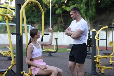 Photo of Young woman exercising with outdoor gym equipment with professional personal trainer outdoors