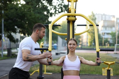 Photo of Young woman exercising with outdoor gym equipment with professional personal trainer outdoors