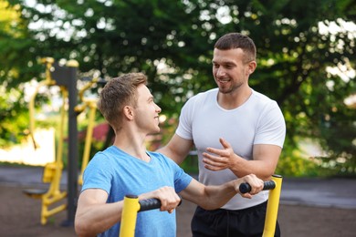 Photo of Young man exercising with outdoor gym equipment with professional personal trainer outdoors