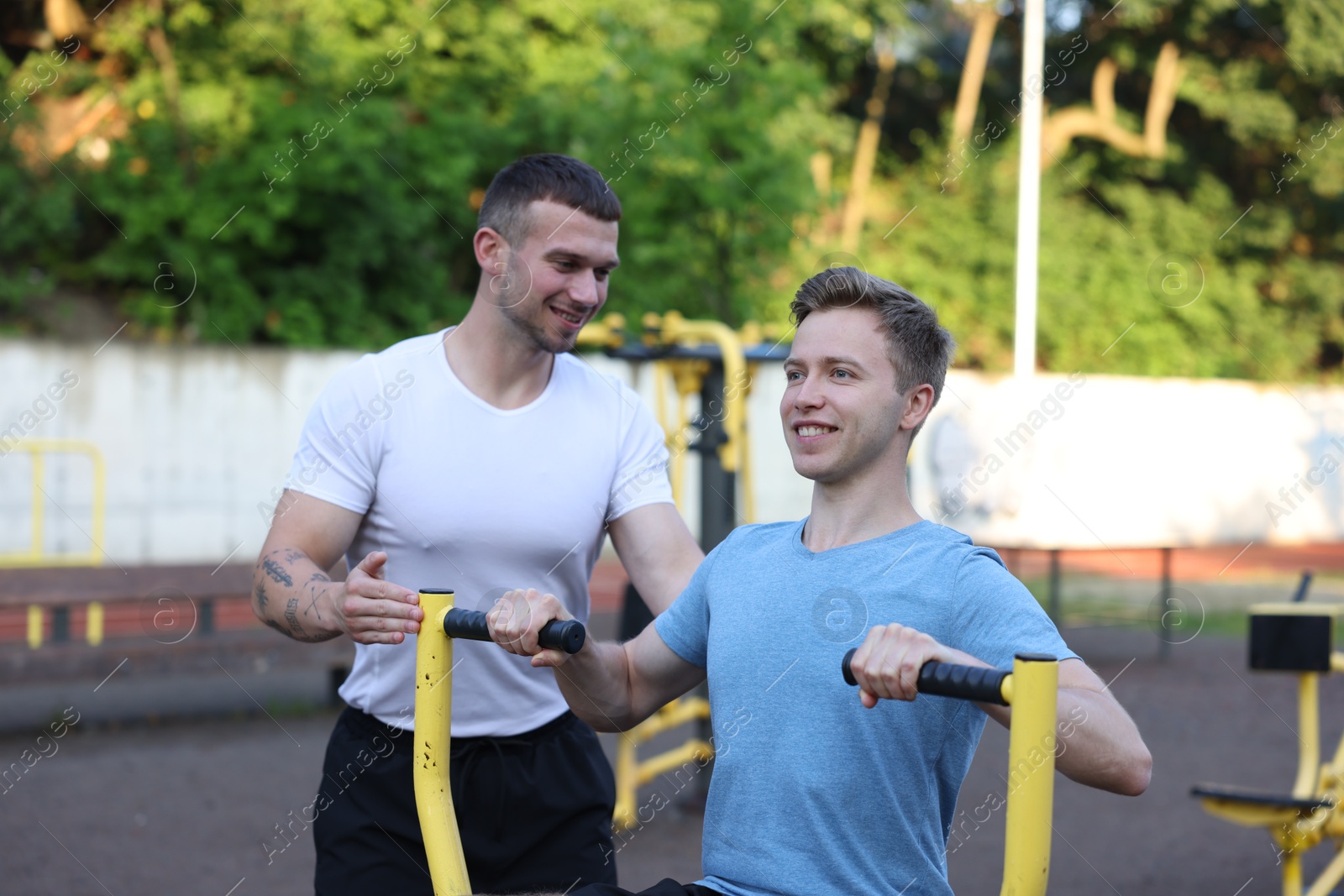 Young man exercising with outdoor gym equipment with professional personal trainer outdoors Photo of Young man exercising with outdoor gym equipment with professional personal trainer outdoors