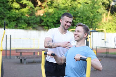 Photo of Young man exercising with outdoor gym equipment with professional personal trainer outdoors