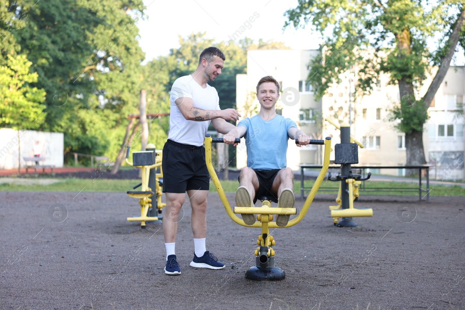 Young man exercising with outdoor gym equipment with professional personal trainer outdoors Photo of Young man exercising with outdoor gym equipment with professional personal trainer outdoors
