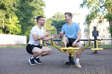 Photo of Young man exercising with outdoor gym equipment with professional personal trainer outdoors