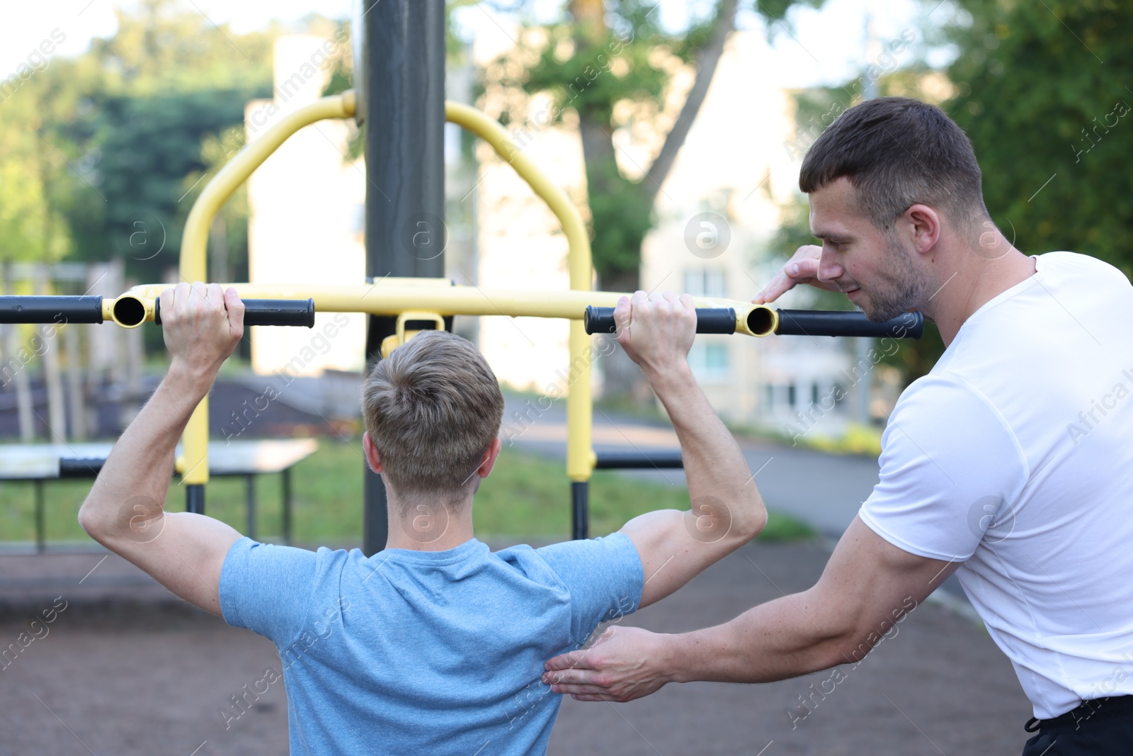 Young man exercising with outdoor gym equipment with professional personal trainer outdoors, back view Photo of Young man exercising with outdoor gym equipment with professional personal trainer outdoors, back view