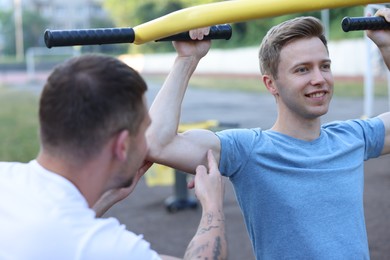 Photo of Young man exercising with outdoor gym equipment with professional personal trainer outdoors
