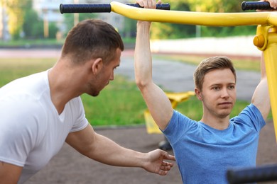 Photo of Young man exercising with outdoor gym equipment with professional personal trainer outdoors