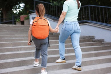Photo of Mother taking her daughter to school outdoors, back view