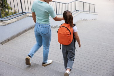 Photo of Mother taking her daughter to school outdoors, back view