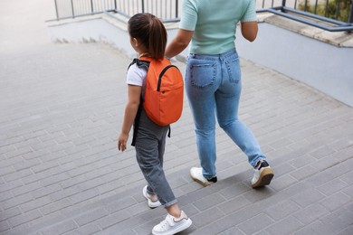 Photo of Mother taking her daughter to school outdoors, back view