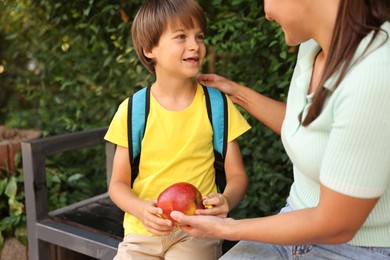 Photo of Mother giving apple to her son while taking him to school outdoors, closeup