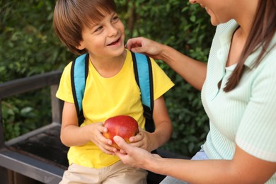 Photo of Mother giving apple to her son while taking him to school outdoors, closeup