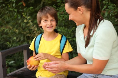 Photo of Mother giving apple to her son while taking him to school outdoors