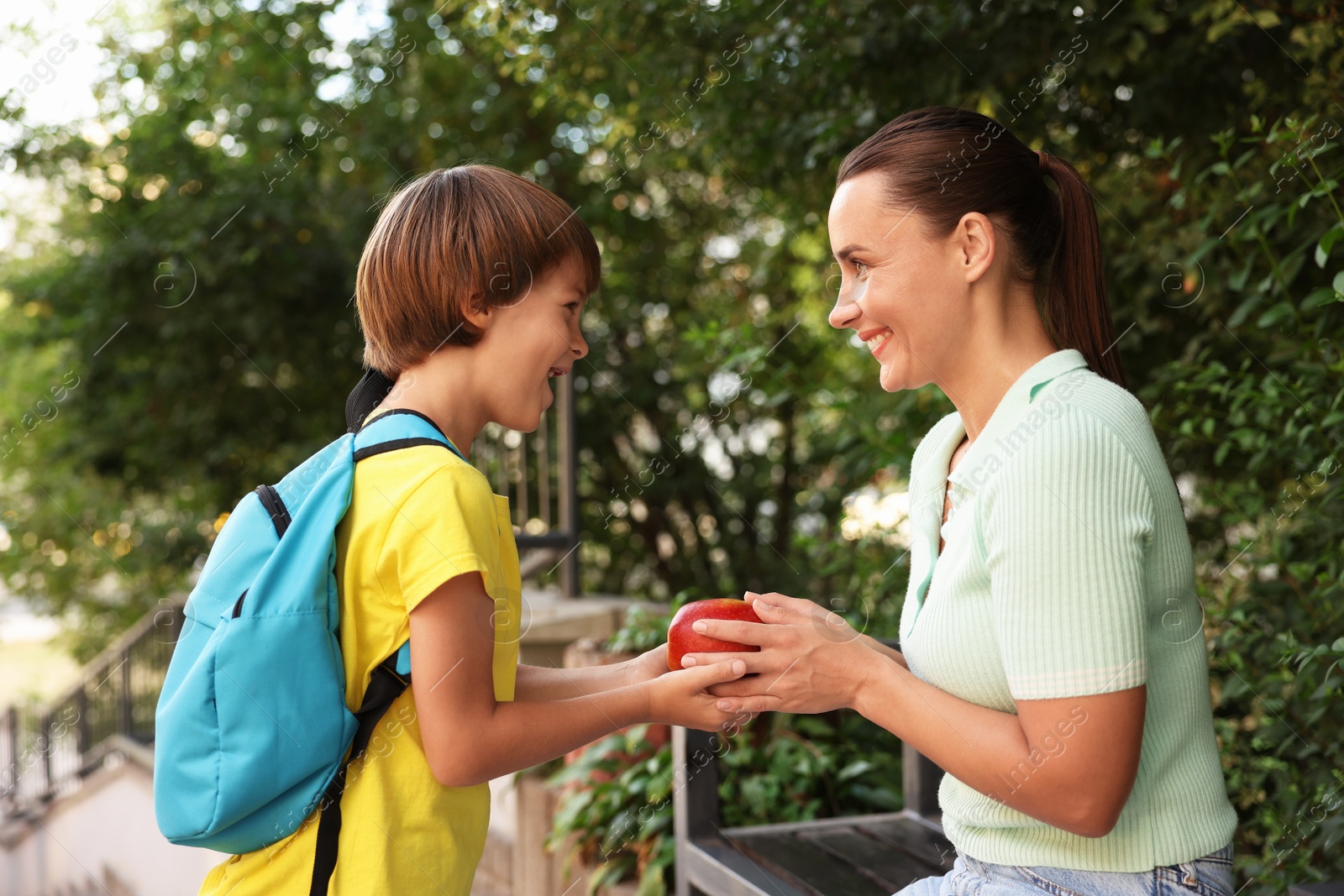Photo of Mother giving apple to her son while taking him to school outdoors