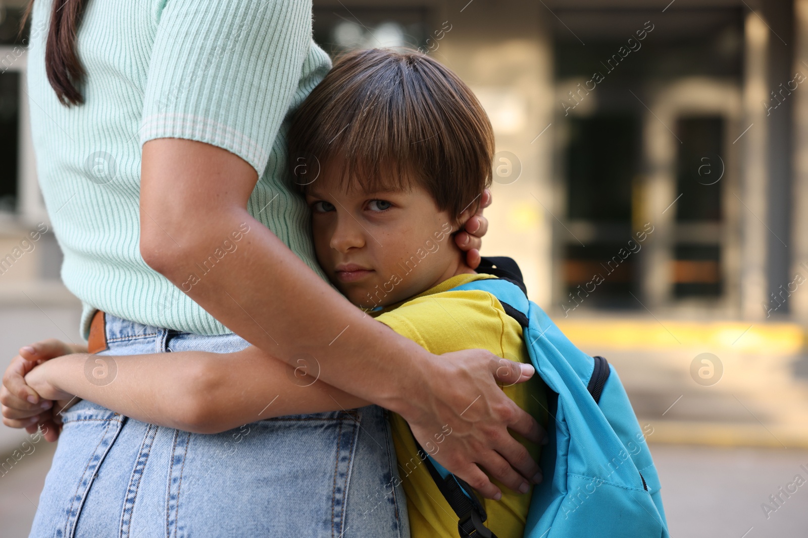 Photo of Mother hugging her son while taking him to school outdoors, closeup