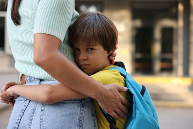 Photo of Mother hugging her son while taking him to school outdoors, closeup