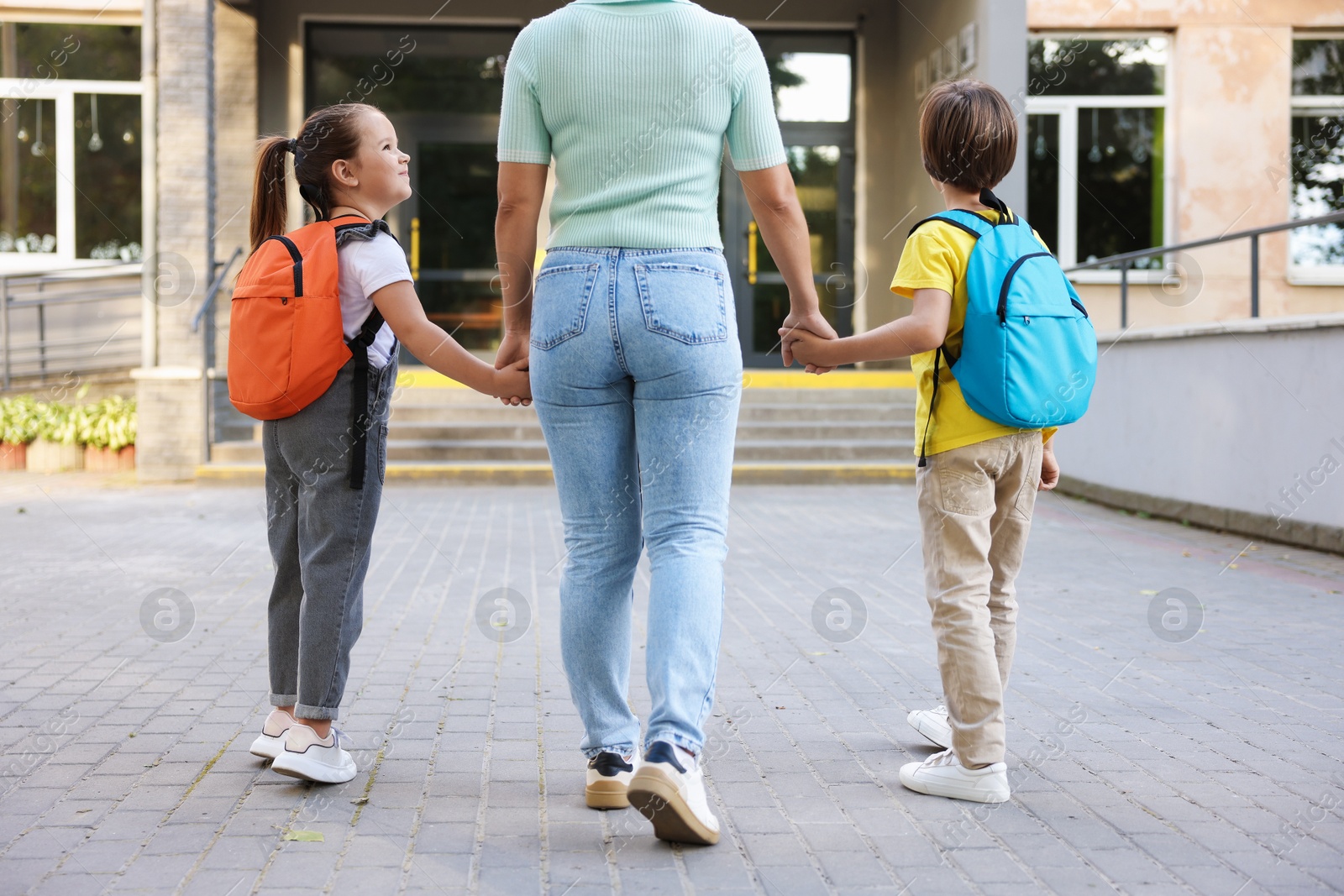 Photo of Mother taking her children to school outdoors, back view