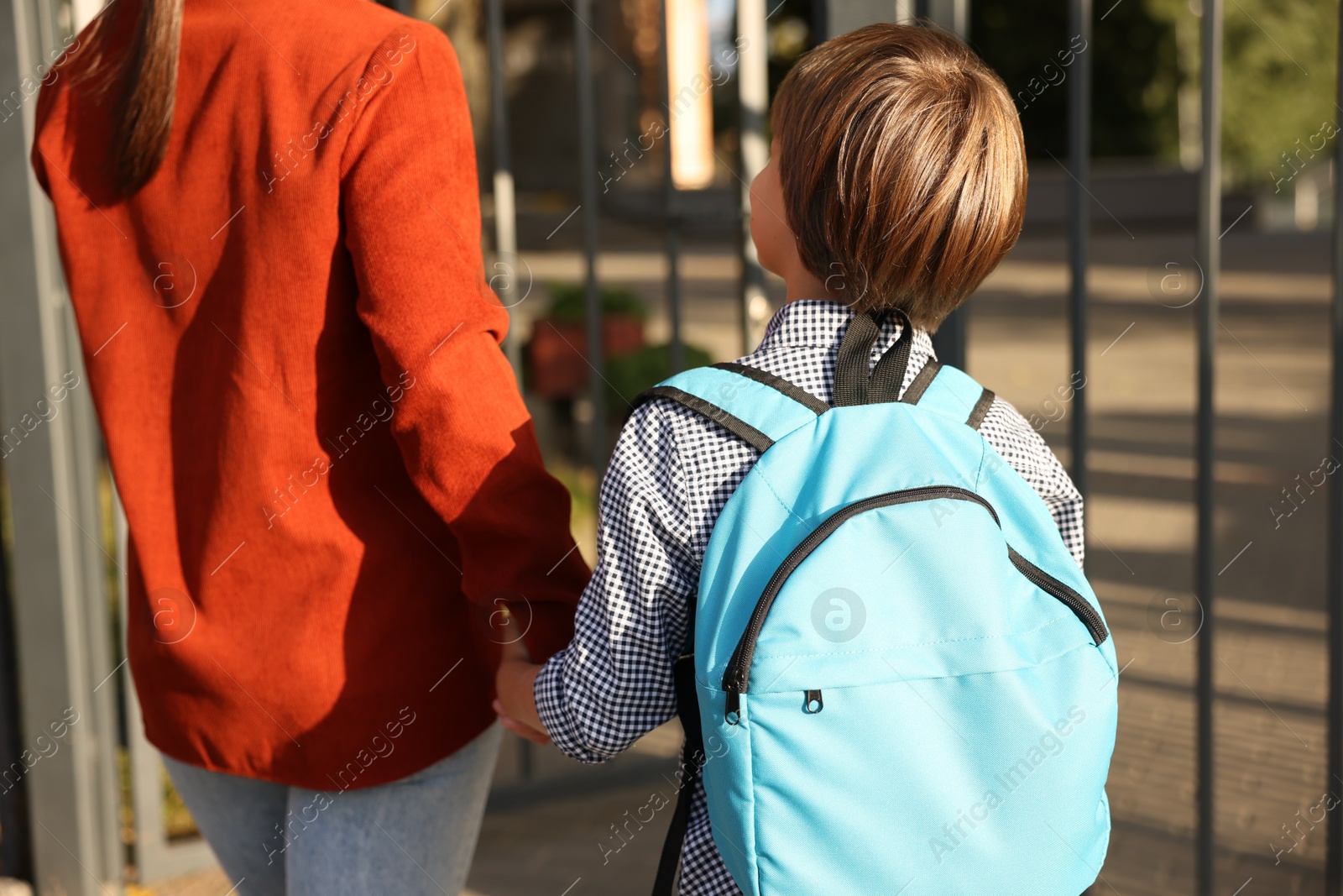 Photo of Mother taking her son to school outdoors, back view