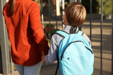 Photo of Mother taking her son to school outdoors, back view