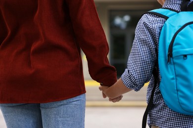 Photo of Mother holding hands with her son and taking him to school outdoors, closeup