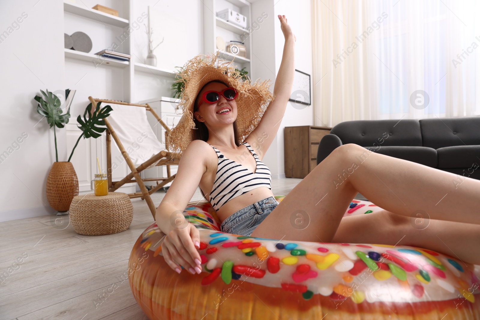 Photo of Happy woman in sunglasses and straw hat with inflatable ring having fun on floor at home. Dreaming about vacation at sea