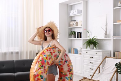 Photo of Happy woman in sunglasses and straw hat with inflatable ring at home. Dreaming about vacation at sea