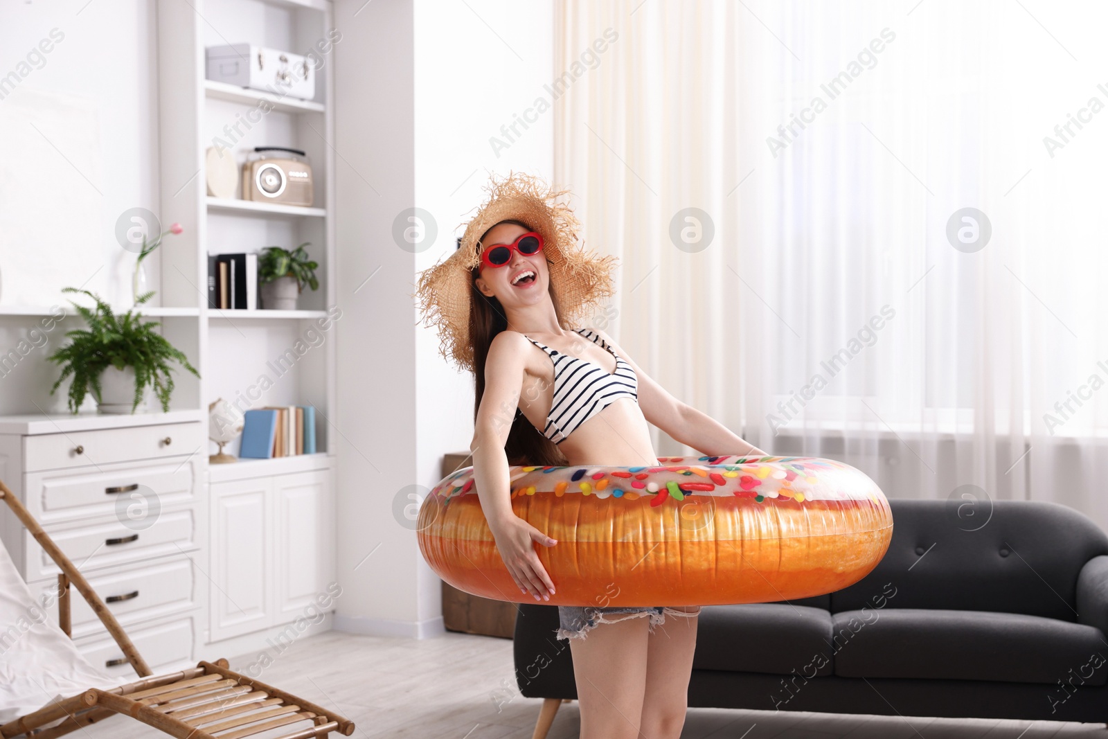 Happy woman in sunglasses and straw hat with inflatable ring having fun at home. Dreaming about vacation at sea Photo of Happy woman in sunglasses and straw hat with inflatable ring having fun at home. Dreaming about vacation at sea