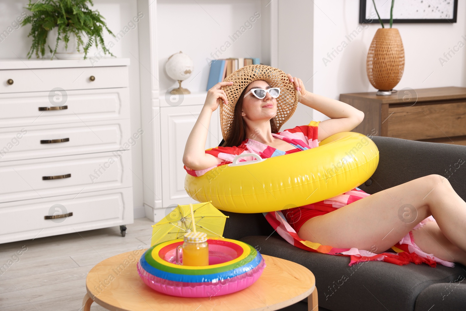 Woman in sunglasses and straw hat with inflatable ring having fun on sofa at home. Dreaming about vacation at sea Photo of Woman in sunglasses and straw hat with inflatable ring having fun on sofa at home. Dreaming about vacation at sea