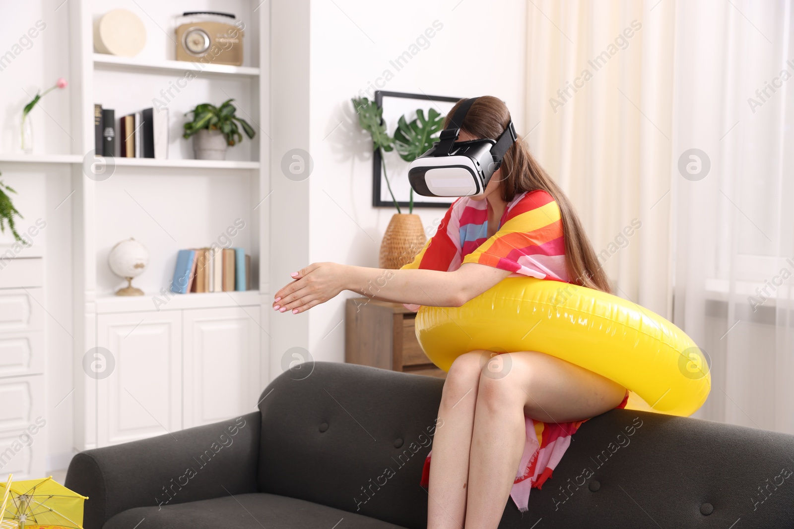 Woman with inflatable ring using virtual reality headset on sofa at home. Dreaming about vacation at sea Photo of Woman with inflatable ring using virtual reality headset on sofa at home. Dreaming about vacation at sea