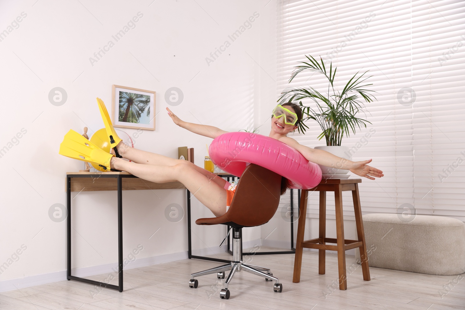 Happy woman in diving mask and flippers with inflatable ring on chair at home. Dreaming about vacation at sea Photo of Happy woman in diving mask and flippers with inflatable ring on chair at home. Dreaming about vacation at sea