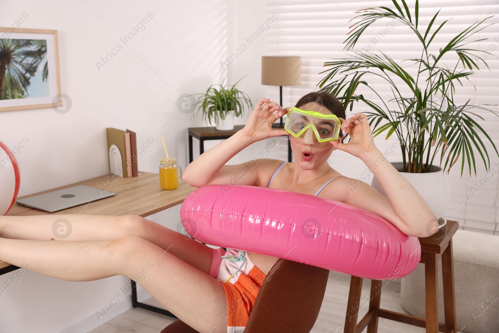 Emotional woman in diving mask with inflatable ring on chair at home. Dreaming about vacation at sea Photo of Emotional woman in diving mask with inflatable ring on chair at home. Dreaming about vacation at sea