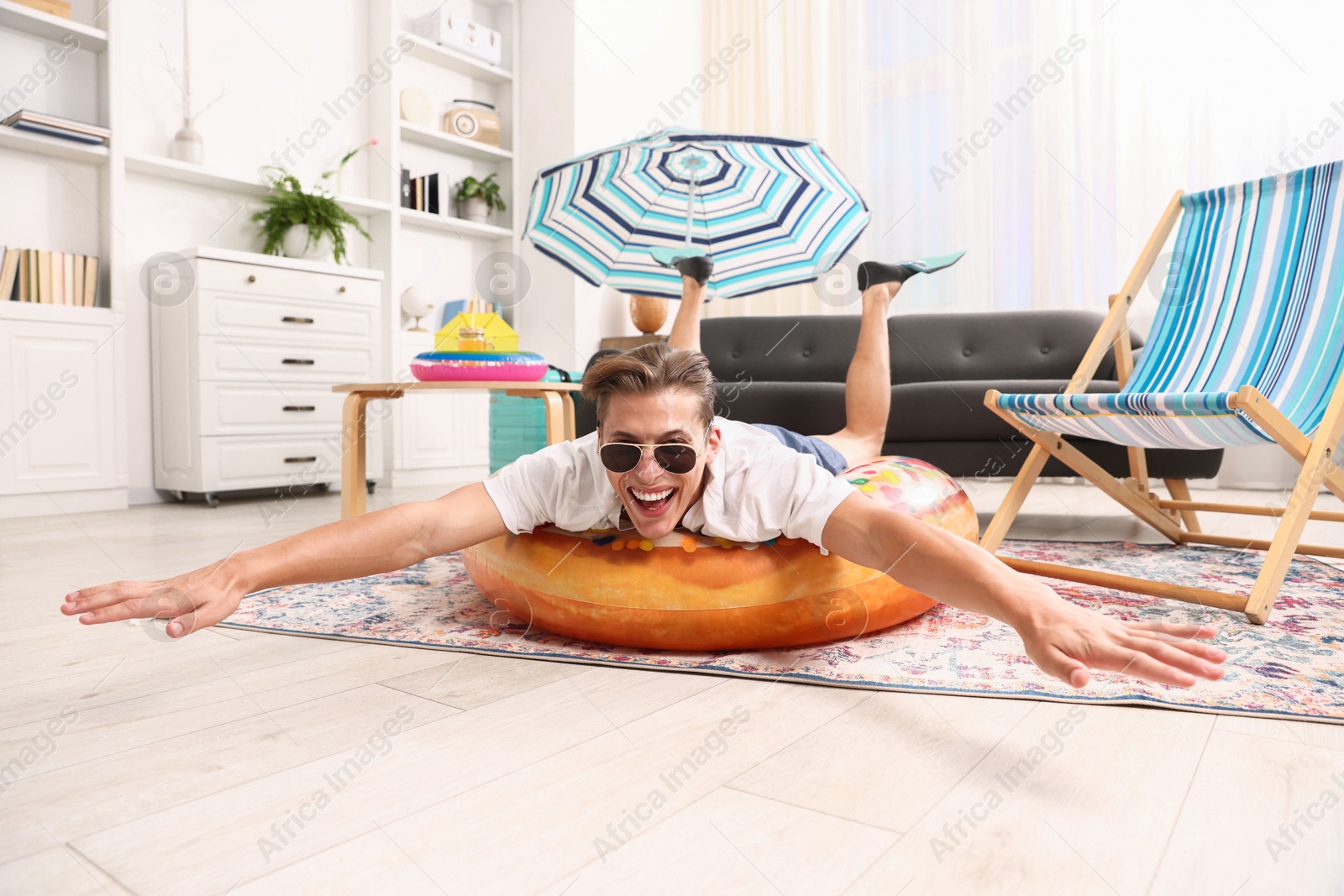 Happy man in sunglasses and flippers with inflatable ring having fun on floor at home. Dreaming about vacation at sea Photo of Happy man in sunglasses and flippers with inflatable ring having fun on floor at home. Dreaming about vacation at sea