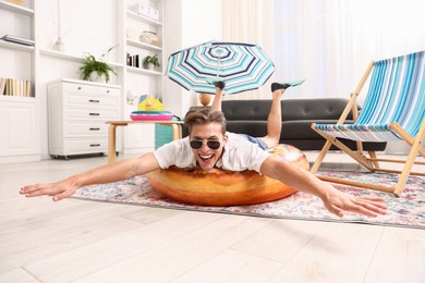 Photo of Happy man in sunglasses and flippers with inflatable ring having fun on floor at home. Dreaming about vacation at sea