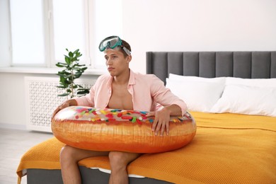 Photo of Frustrated man with diving mask and inflatable ring on bed at home. Dreaming about vacation at sea