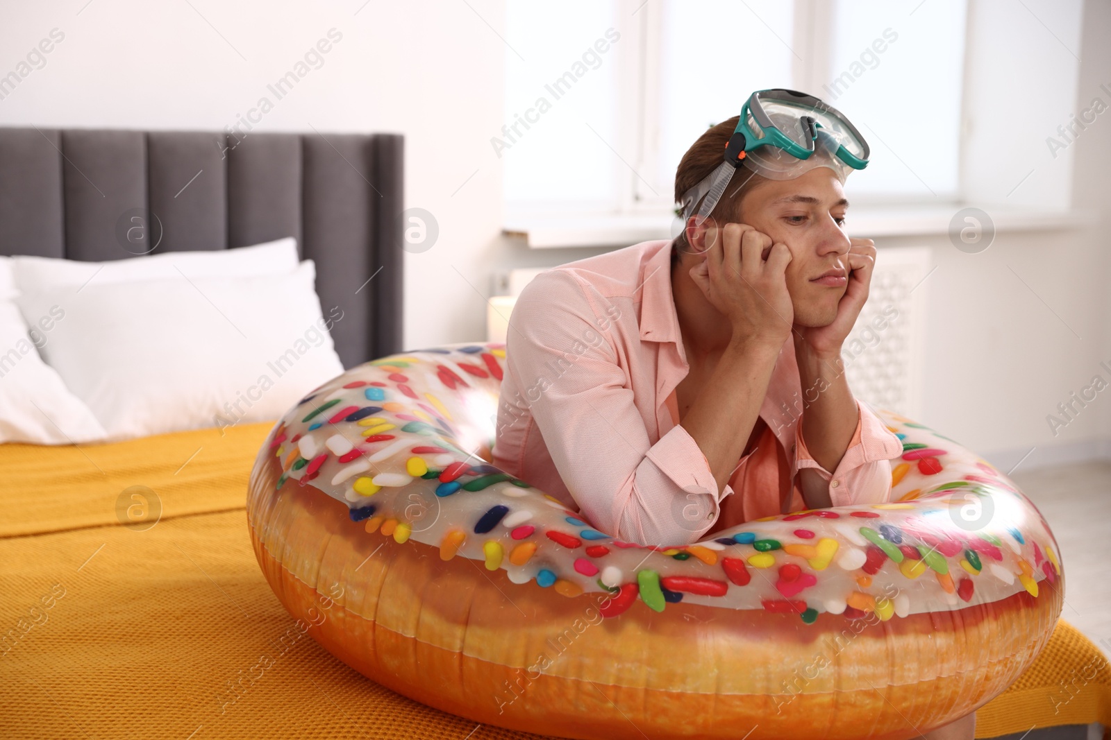 Frustrated man with diving mask and inflatable ring on bed at home. Dreaming about vacation at sea Photo of Frustrated man with diving mask and inflatable ring on bed at home. Dreaming about vacation at sea