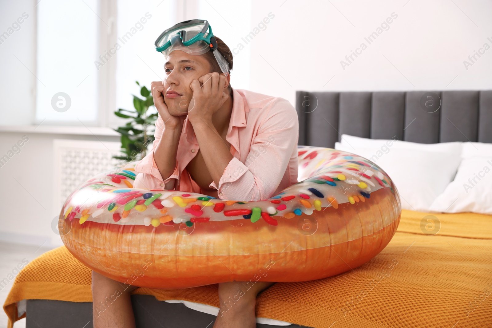 Frustrated man with diving mask and inflatable ring on bed at home. Dreaming about vacation at sea Photo of Frustrated man with diving mask and inflatable ring on bed at home. Dreaming about vacation at sea