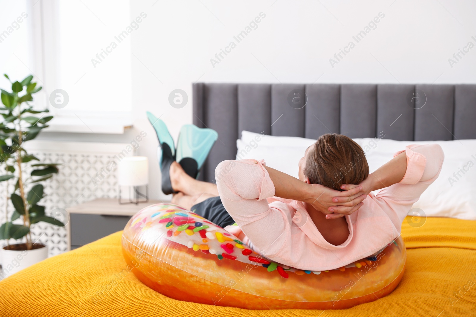 Man in flippers with inflatable ring on bed at home. Dreaming about vacation at sea Photo of Man in flippers with inflatable ring on bed at home. Dreaming about vacation at sea