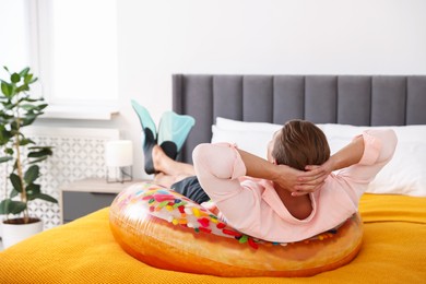 Photo of Man in flippers with inflatable ring on bed at home. Dreaming about vacation at sea