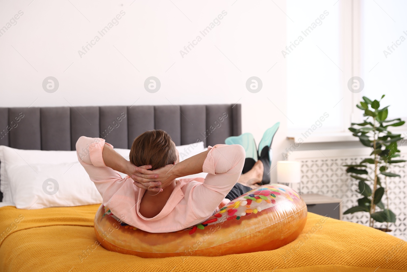Man in flippers with inflatable ring on bed at home. Dreaming about vacation at sea Photo of Man in flippers with inflatable ring on bed at home. Dreaming about vacation at sea