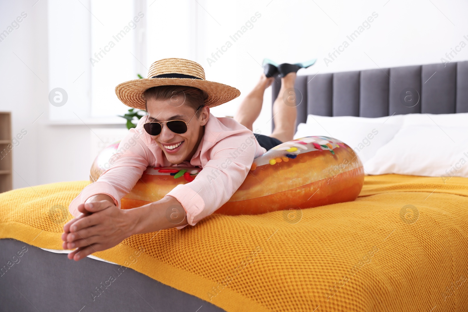 Happy man in straw hat and sunglasses with inflatable ring on bed at home. Dreaming about vacation at sea Photo of Happy man in straw hat and sunglasses with inflatable ring on bed at home. Dreaming about vacation at sea