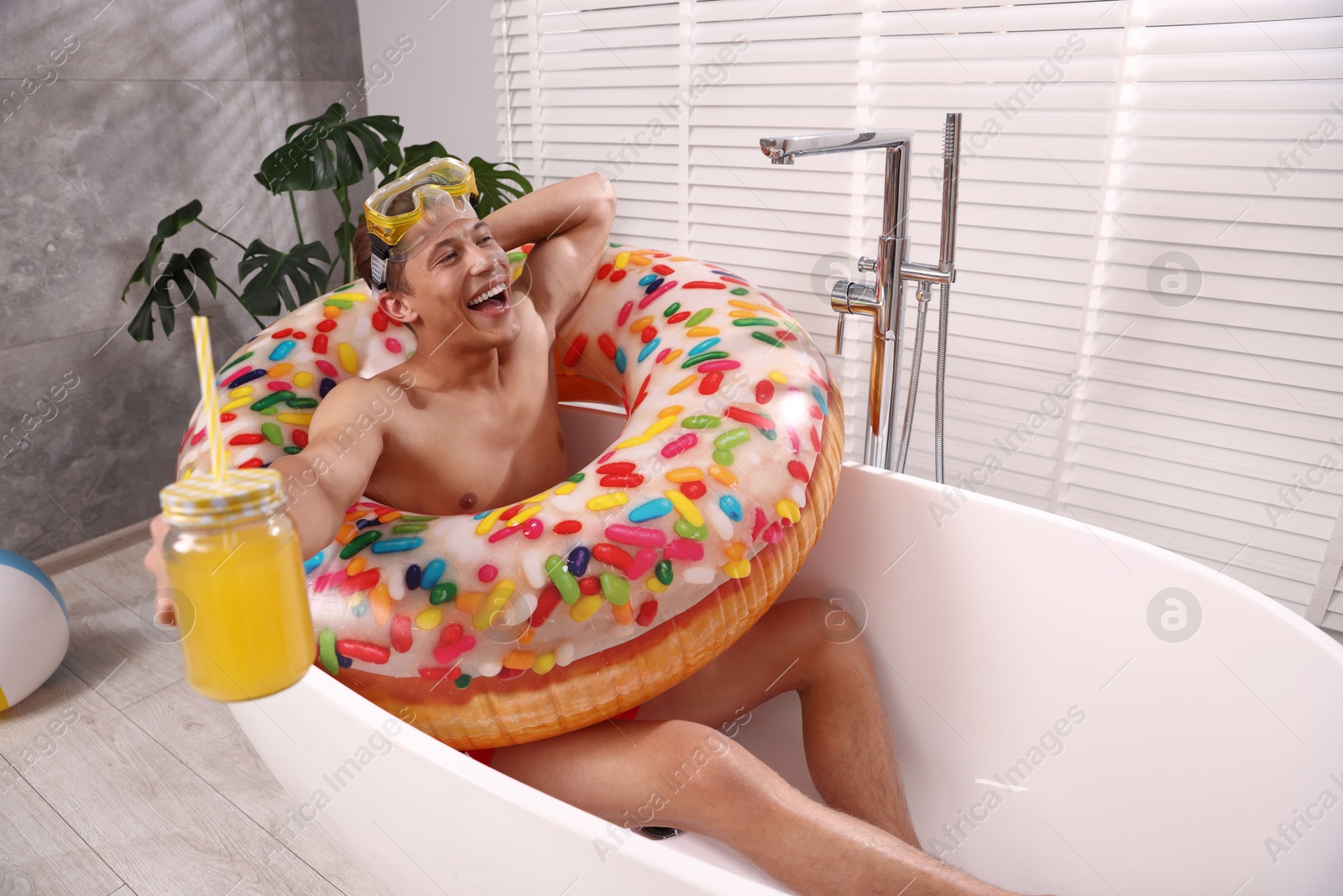 Happy man with diving mask, mason jar of juice and inflatable ring chilling in bathtub at home. Dreaming about vacation at sea Photo of Happy man with diving mask, mason jar of juice and inflatable ring chilling in bathtub at home. Dreaming about vacation at sea